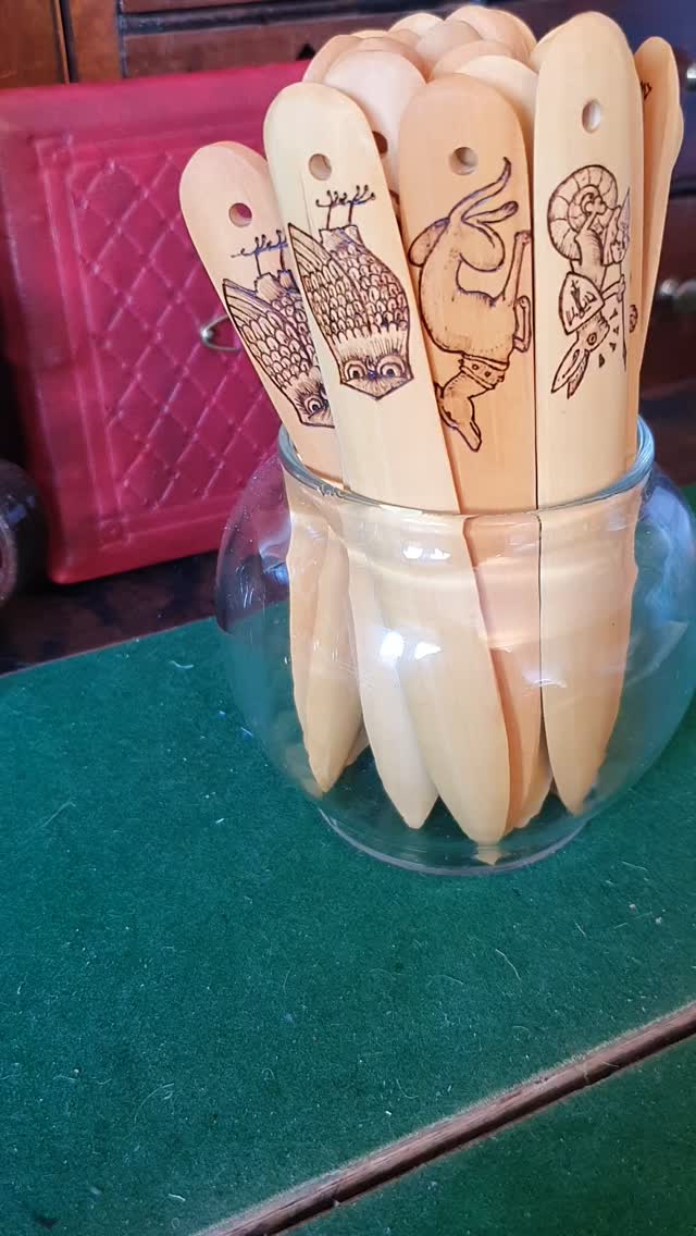 Just the rope twist tails now to add to these pyrography bonefolders. Here's a gentle video of me removing excess oil from the oiling process before I let them dry and add the cord. These will be available at my next couple of fairs, either alone or as part of a bookbinding kit.

[Video description: one after another a wooden bonefolder is removed from a jar and wiped down with a clean cloth before being shown to the camera so the pyrography decoration is visible. Images include an owl, a greyhound, a dragon, and a hair riding a Snail with a man's head.]