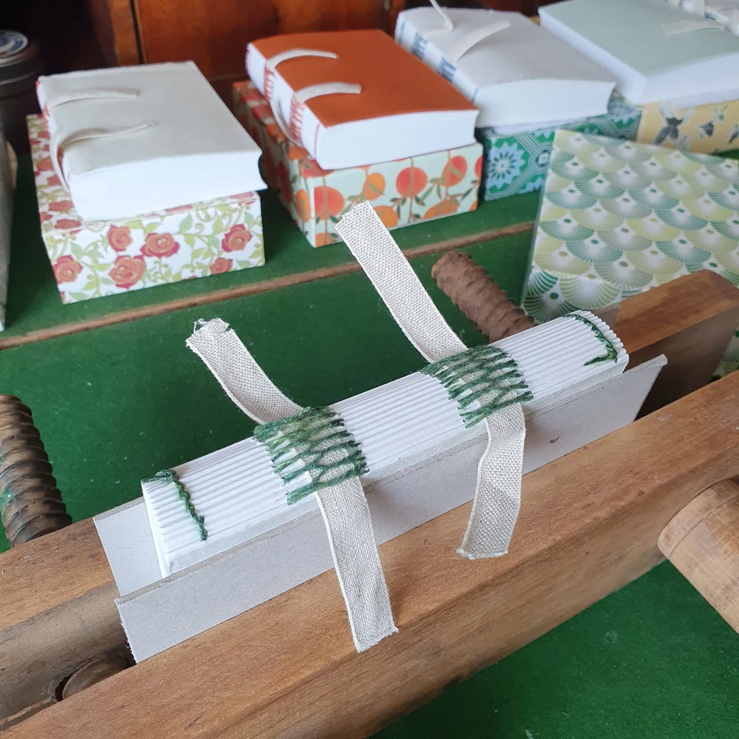 Picked up an old WIP project between the commission and class prep. It's an interesting mix of remembering in slow motion what the original plan was, and taking it in a slightly different direction.

[Image description: a book is sat in a press waiting for its spine linings. In the background are visible other books, each sitting on a different decoratively patterned box.]