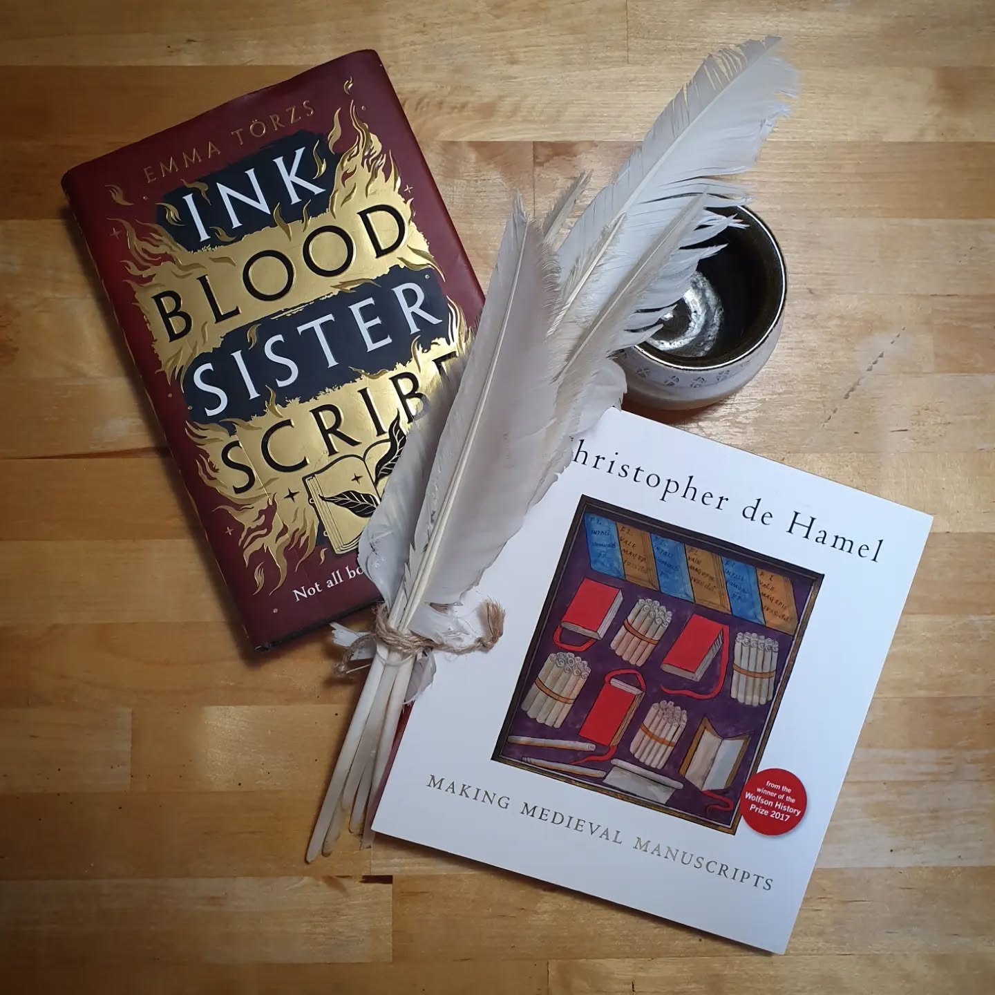 A new Sunday shelfie series I'm starting today, we shall see how long it lasts. What books does a medievalist bookbinder have on her shelves? Today, One fiction, one non-fiction.

The fiction: Ink Blood Sister Scribe by Emma Törzs, bought for me as a Christmas gift by my sister. I found this a light, entertaining read and the idea of magically scribed books is always fun. Despite the medieval sounding title and cover imagery, it is very much set in present day but with an organisation of magical book collectors that have existed through the ages.

To pair

The non-fiction: Making Medieval Manuscripts by Christopher de Hamel. An entry level introduction into manuscript production, this book gives an overview of the process, alongside imagery from the Bodleian of finished and (my favourites from this book) part finished manuscripts and discussion of the costs and crafters involved.

[Image description: two books posed with goose feathers and a replica medieval ceramic bowl.]